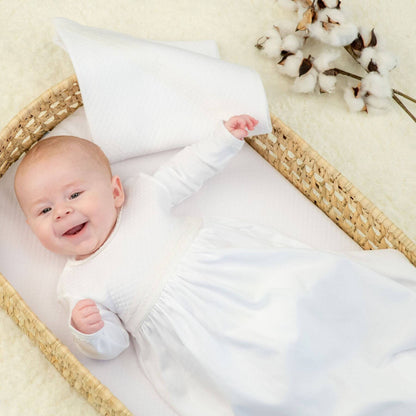 Baby in Bebe Sweeny Baby White Quilted Cotton Gown lying in a basket with white bedding and cotton flowers in the background