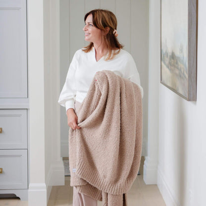 Woman holding Saranoni Bamboni® Throw Blanket in a room with light-colored walls and a painting.