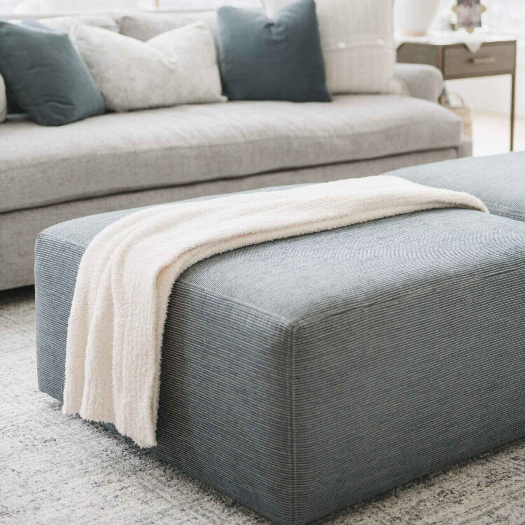 Gray ottoman with Saranoni Bamboni® Throw Blanket on top, in a living room setting.
