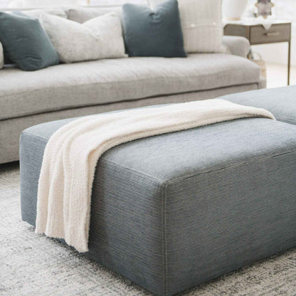 Gray ottoman with Saranoni Bamboni® Throw Blanket on top, in a living room setting.
