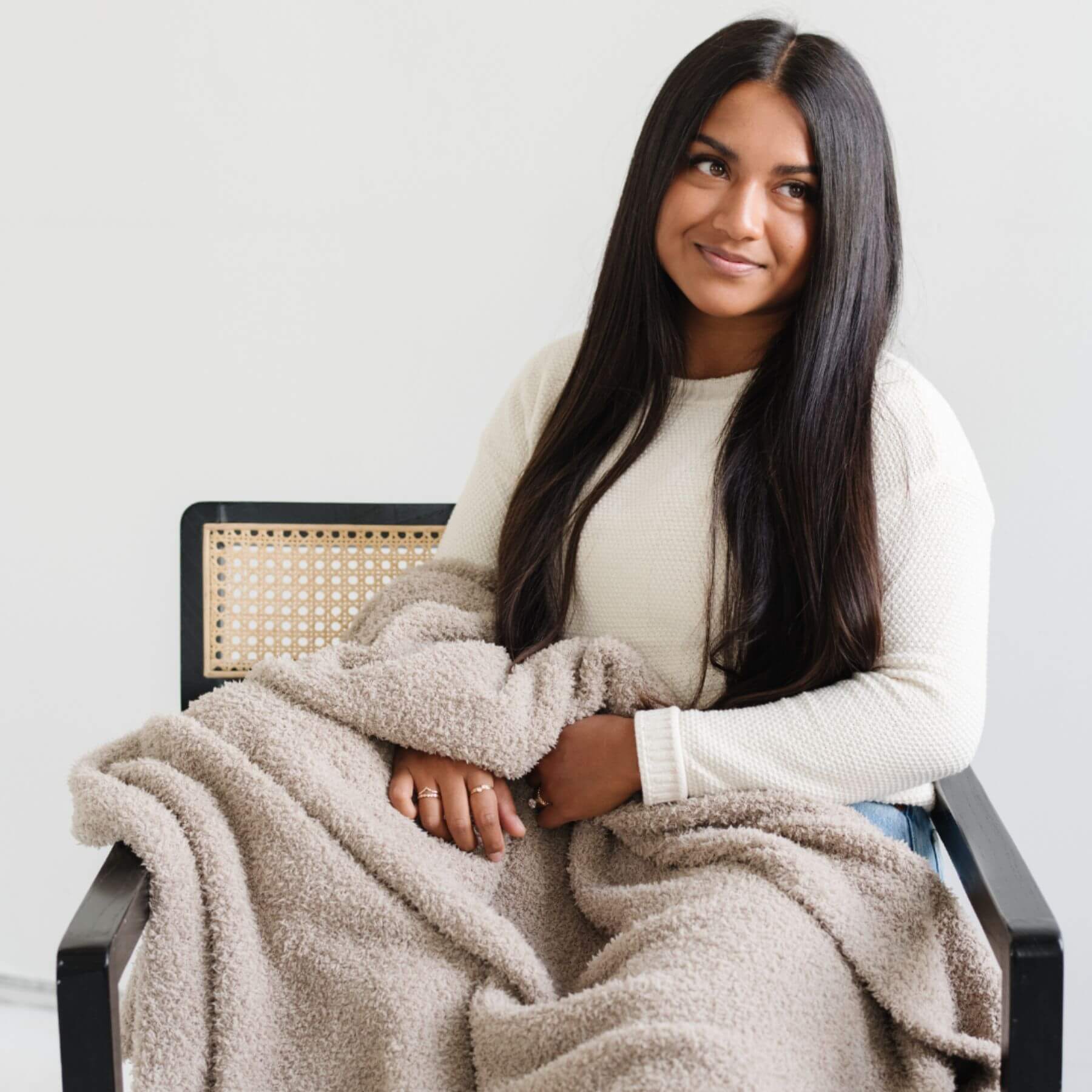 Woman sitting on a chair with Saranoni Bamboni® Throw Blanket draped over her, wearing a white sweater.