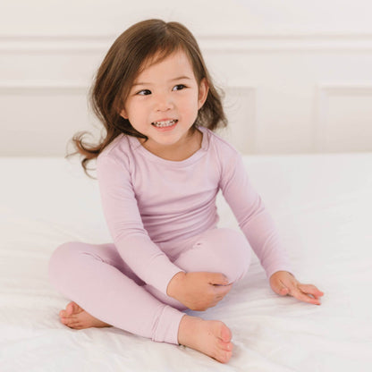 Child wearing Dreamland Baby Toddler/Kids Bamboo Pajamas - Blush sitting on a white bed