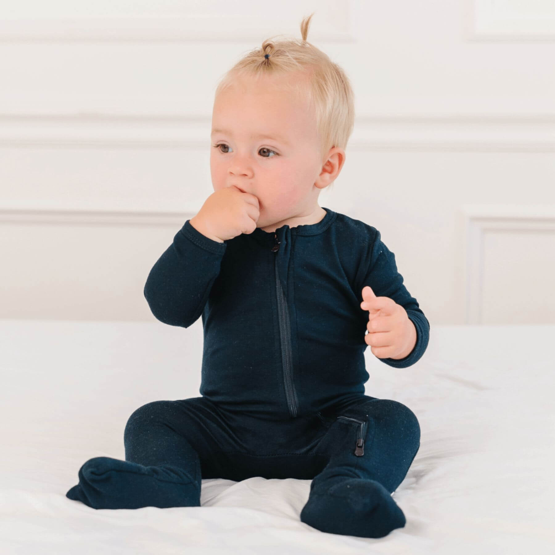 Baby wearing Dreamland Baby Bamboo Pajamas w/ DreamCuffs® - Black sitting on a white bed.