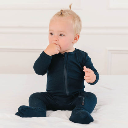 Baby wearing Dreamland Baby Bamboo Pajamas w/ DreamCuffs® - Black sitting on a white bed.