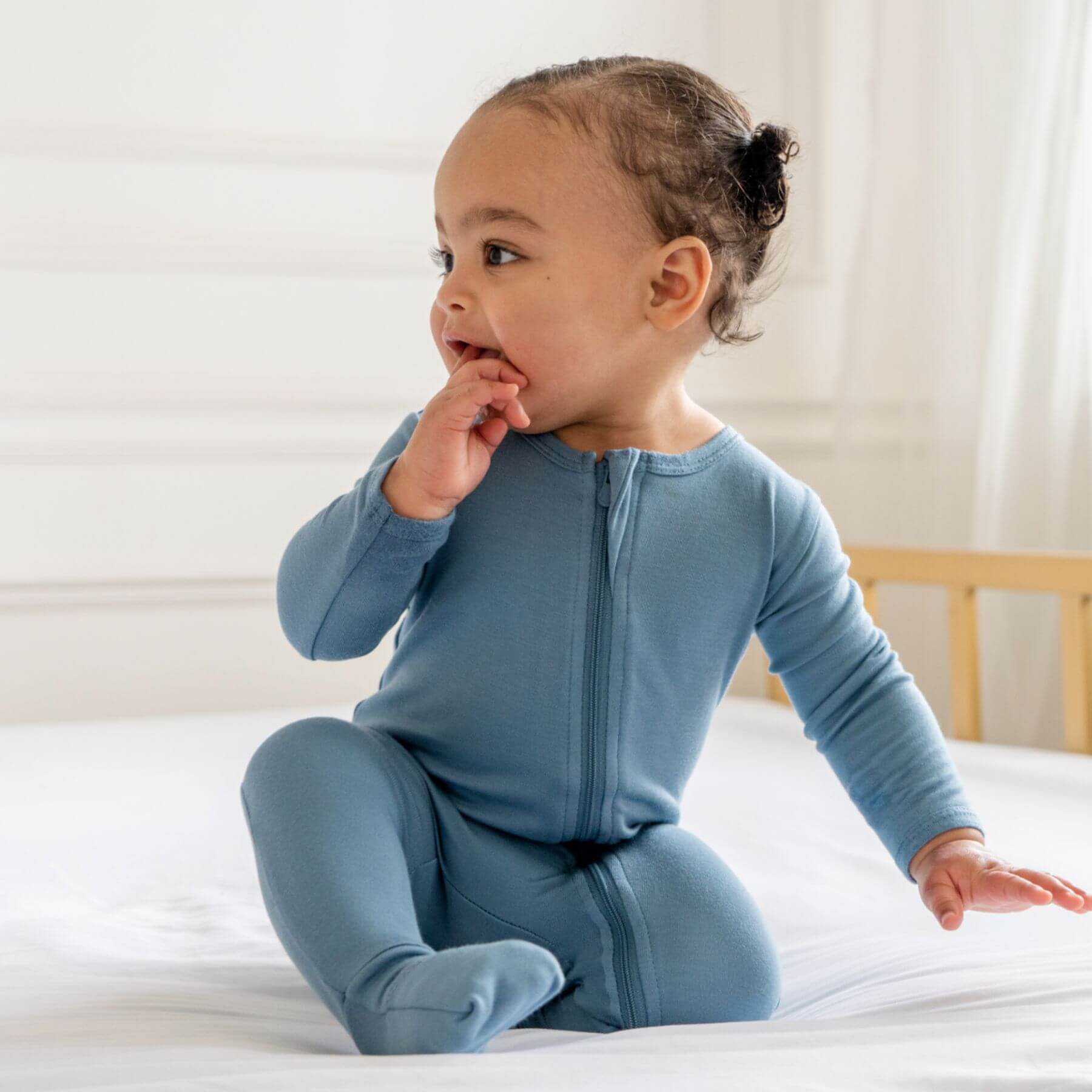 Baby in Dreamland Baby Bamboo Pajamas w/ DreamCuffs® - Blue sitting on a bed