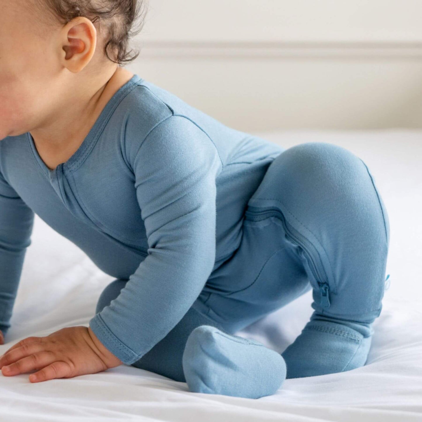 Baby in Dreamland Baby Bamboo Pajamas w/ DreamCuffs® - Blue crawling on a white surface