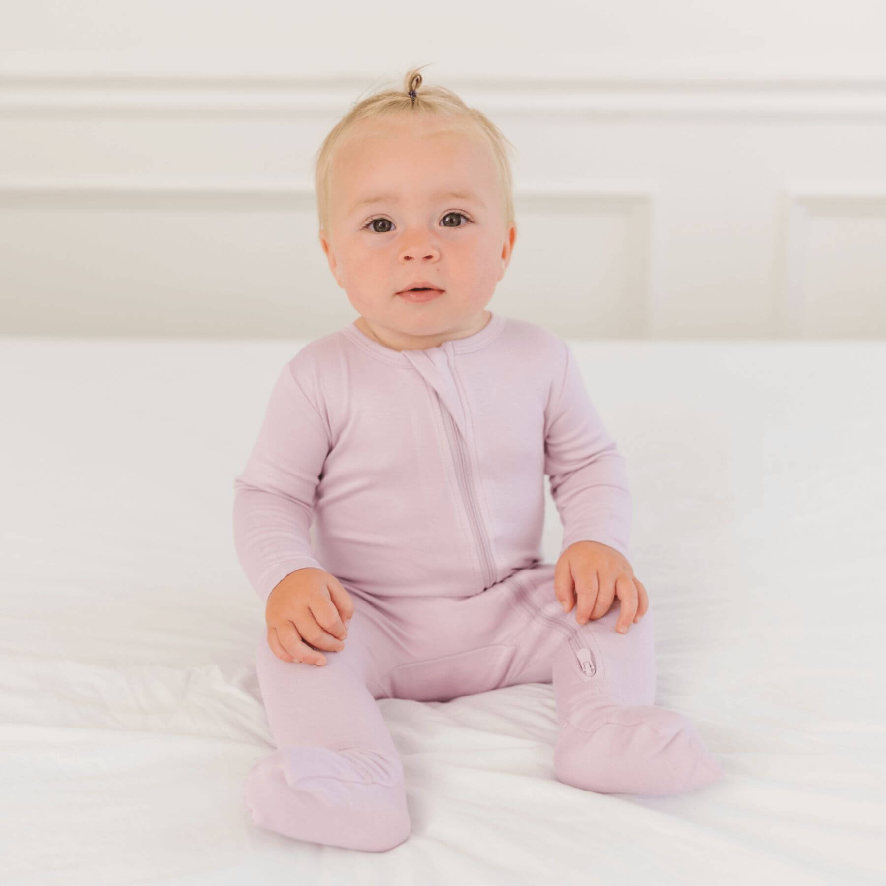 Baby wearing Dreamland Baby Bamboo Pajamas w/ DreamCuffs® - Blush sitting on a white surface