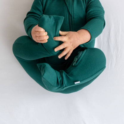 Person wearing Dreamland Baby Bamboo Pajamas w/ DreamCuffs® - Forest sitting on a white surface