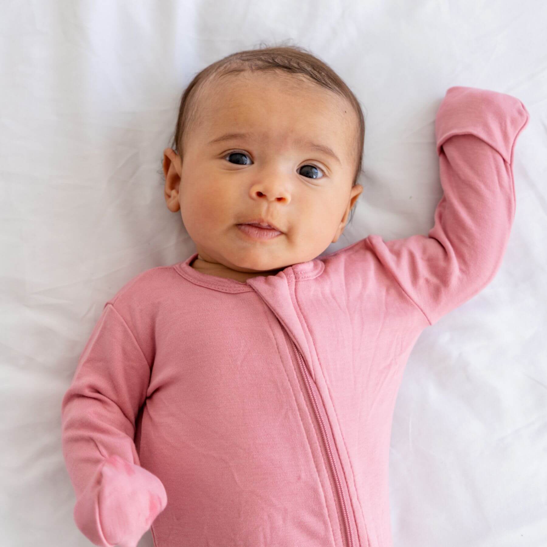 Baby wearing Dreamland Baby Bamboo Pajamas w/ DreamCuffs® - Rose lying on a white surface