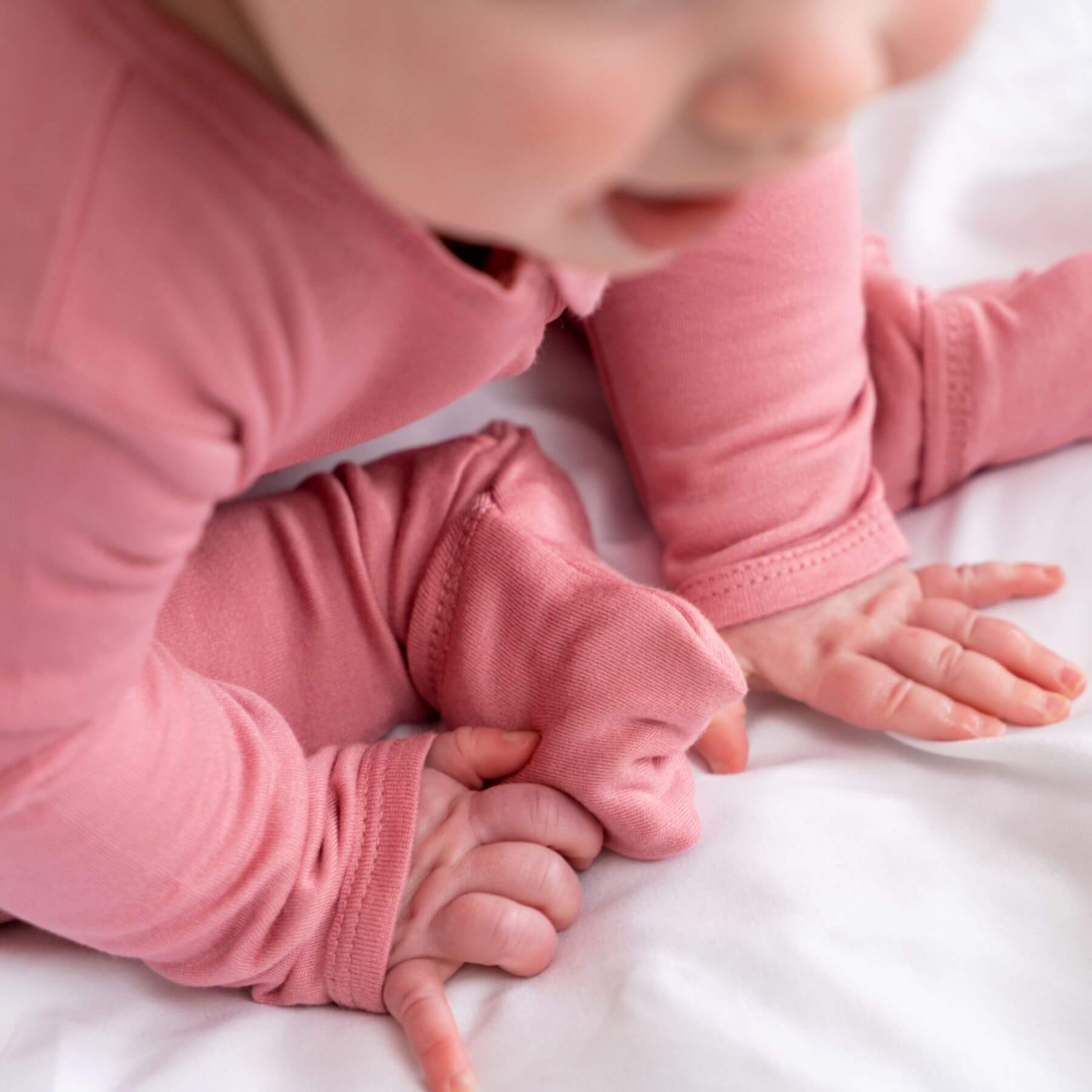 Baby in Dreamland Baby Bamboo Pajamas w/ DreamCuffs® - Rose lying on a white surface