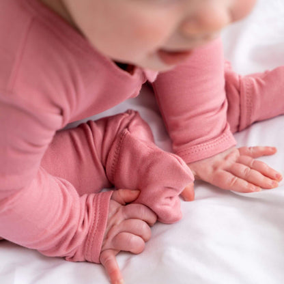 Baby in Dreamland Baby Bamboo Pajamas w/ DreamCuffs® - Rose lying on a white surface