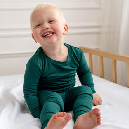 Child wearing Dreamland Baby Toddler/Kids Bamboo Pajamas - Forest Green sitting on a bed