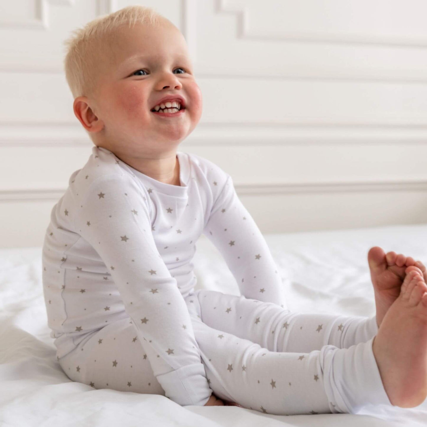 Child wearing Dreamland Baby Toddler/Kids Bamboo Pajamas - Grey Star sitting on a bed.