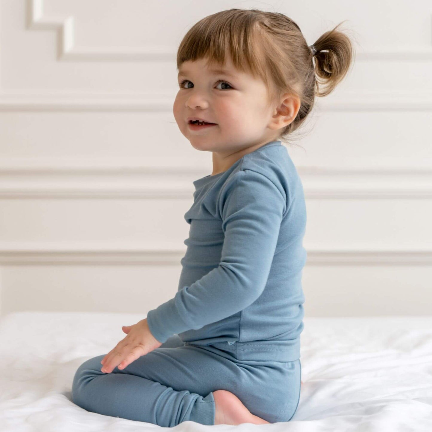 Child wearing a blue pajamas sitting on a white surface.