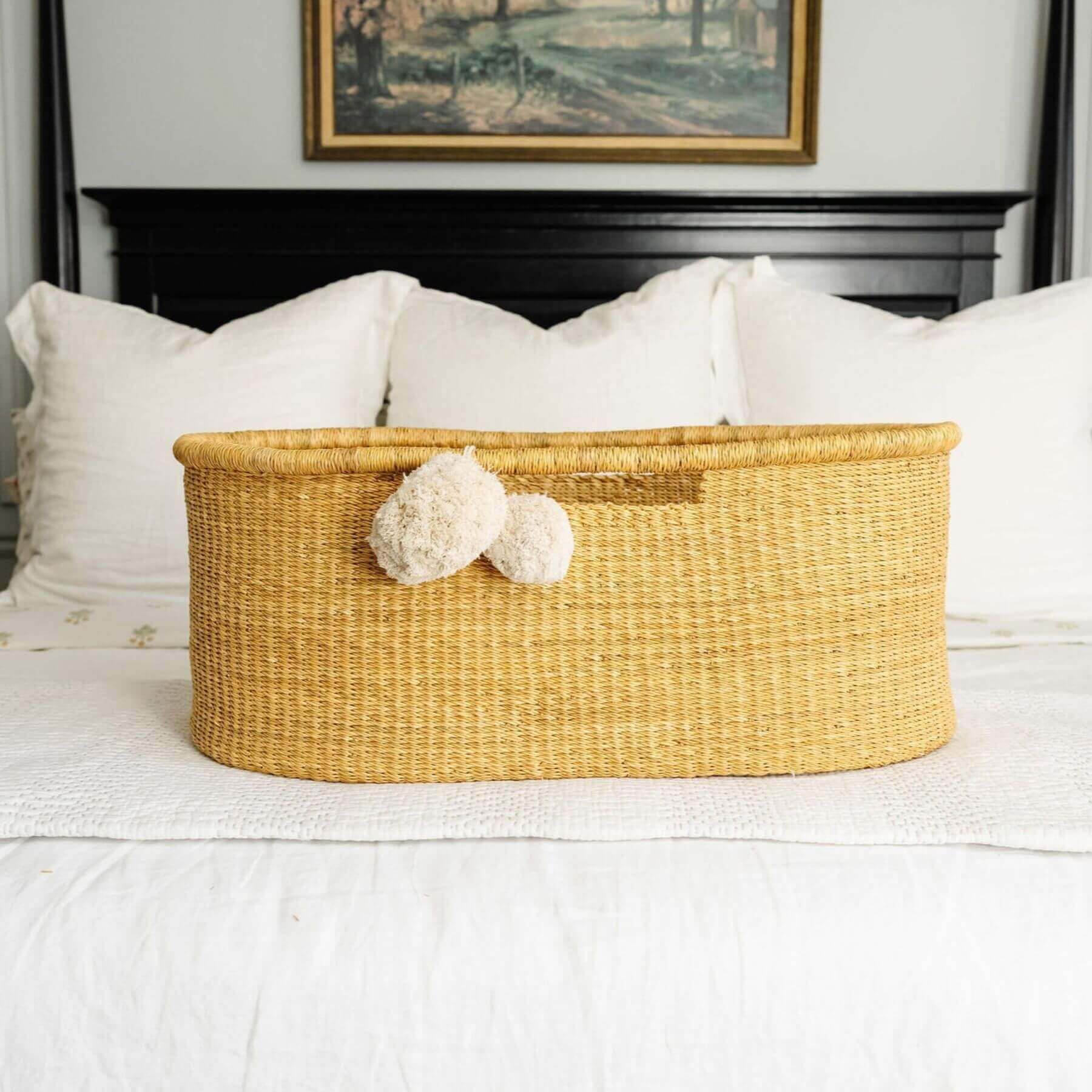 African Moses Basket No Hood Inset Handle on a bed with white bedding and a framed picture in the background.