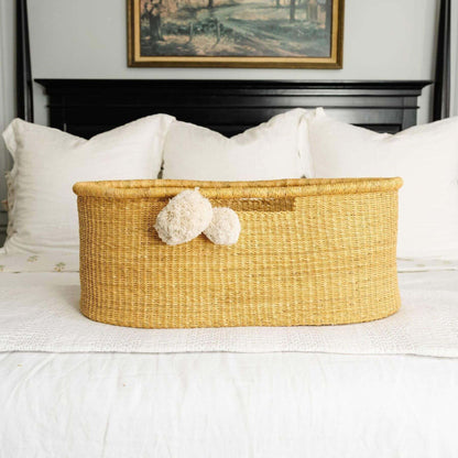 African Moses Basket No Hood Inset Handle on a bed with white bedding and a framed picture in the background.