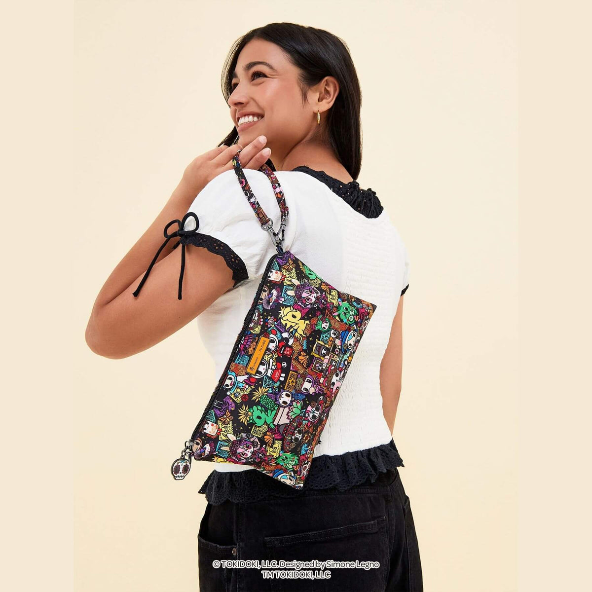 A woman wearing a white top and black skirt carriestokidoki Be Quick Crossbody Diaper Bag Accessory – Dia de los Muertos