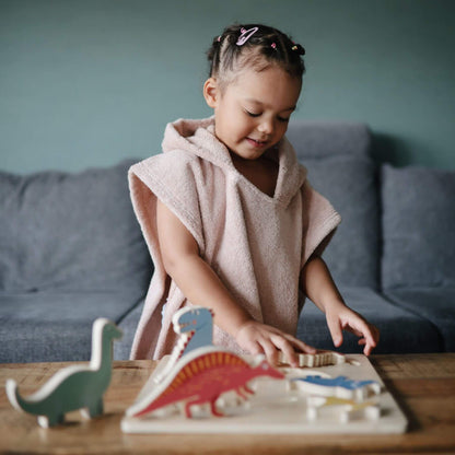 Child in Mushie Bear Poncho Towel playing with wooden dinosaur toys on a table