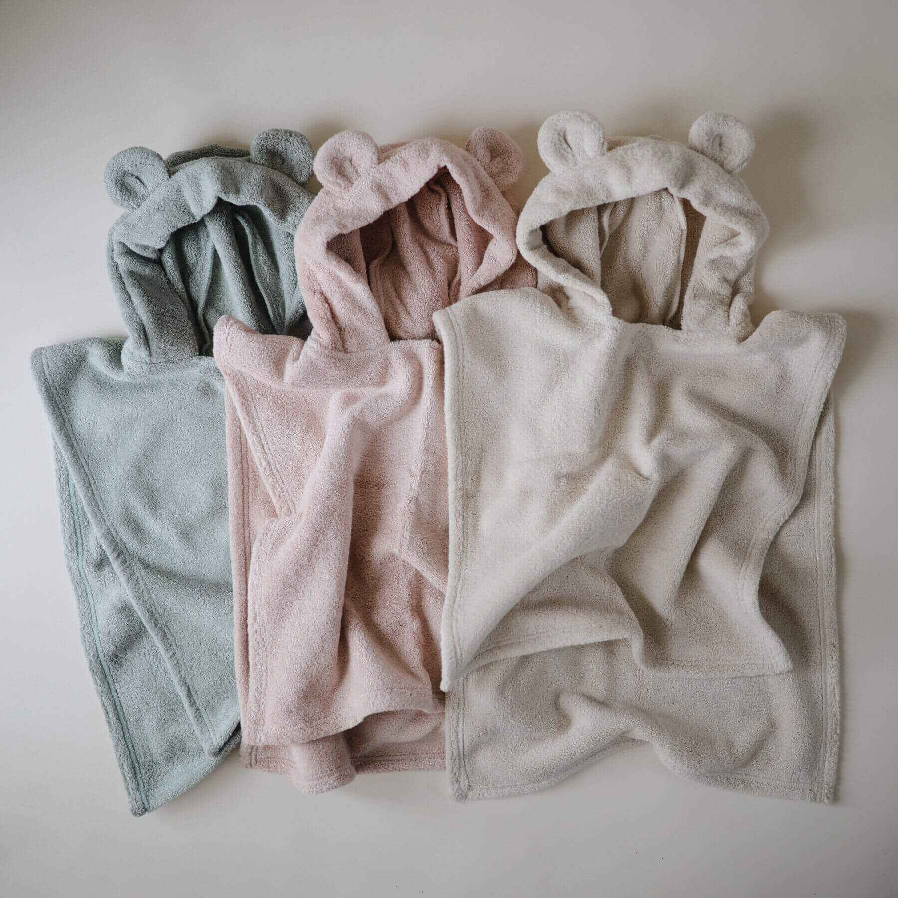 Mushie Bear Poncho Towels in different colors arranged on a light background