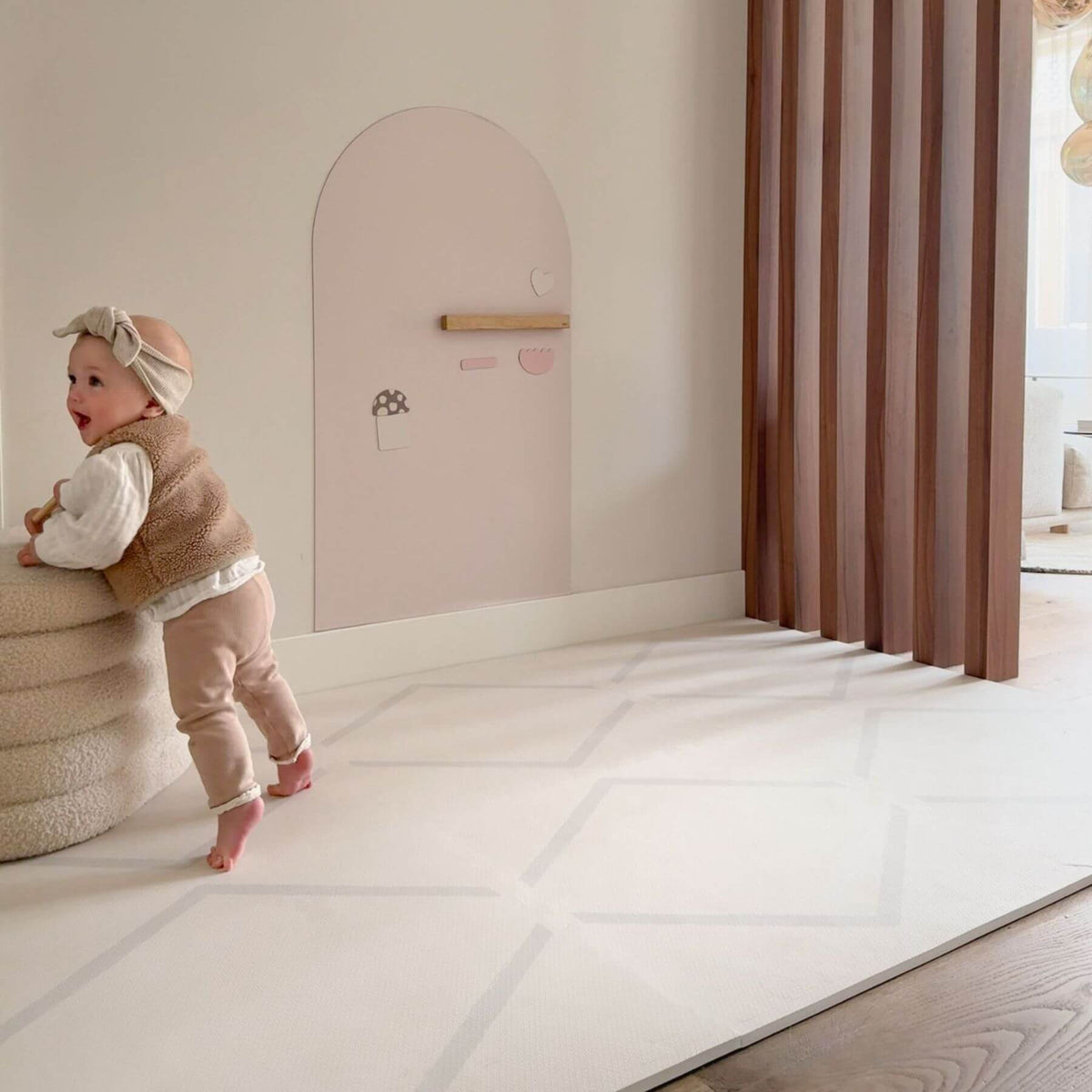 Child standing next to a pink wall with a small door in a room with Eeveve Beni Cashmere Play Mat