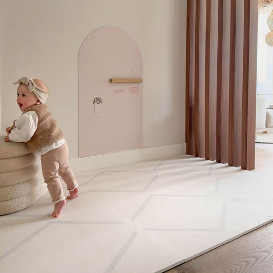 Child standing next to a pink wall with a small door in a room with Eeveve Beni Cashmere Play Mat