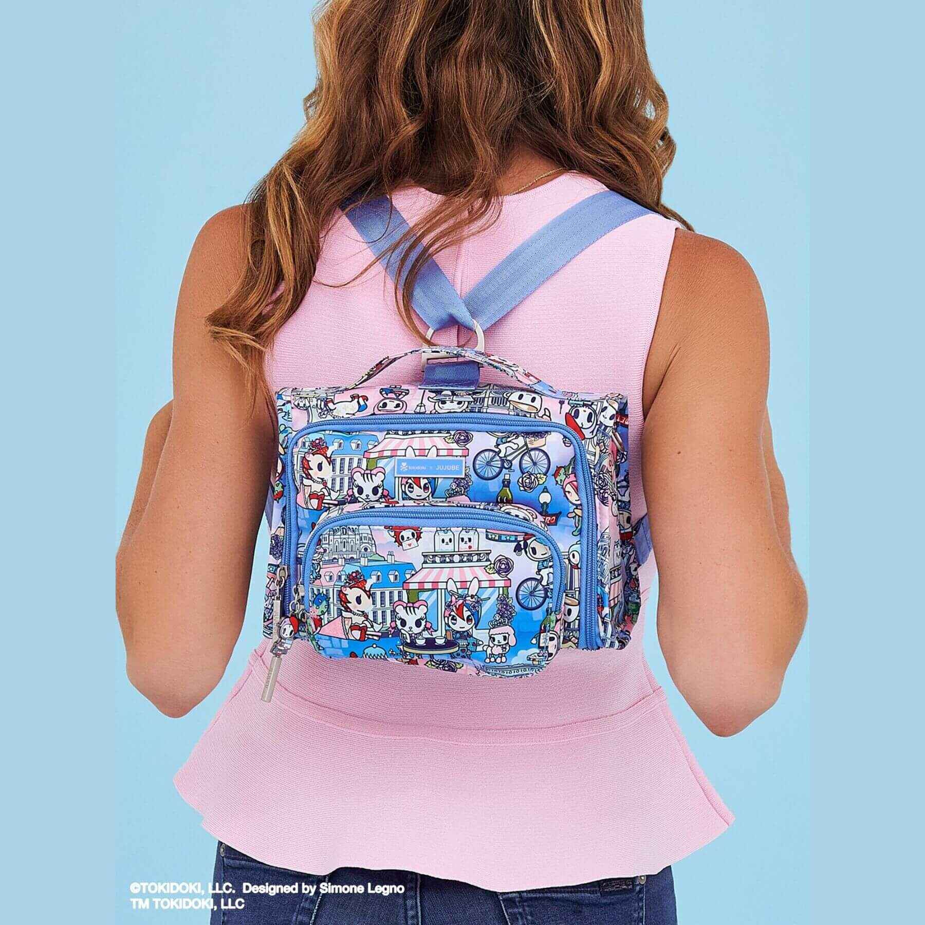 Person wearing tokidoki The Bestie Small Messenger Handbag - C'est la vie à Paris on a light blue background