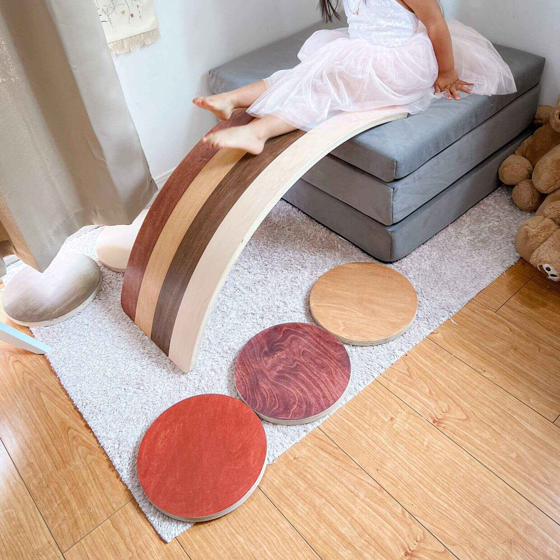 Wooden balance board on a rug with a child sitting on it in a room.