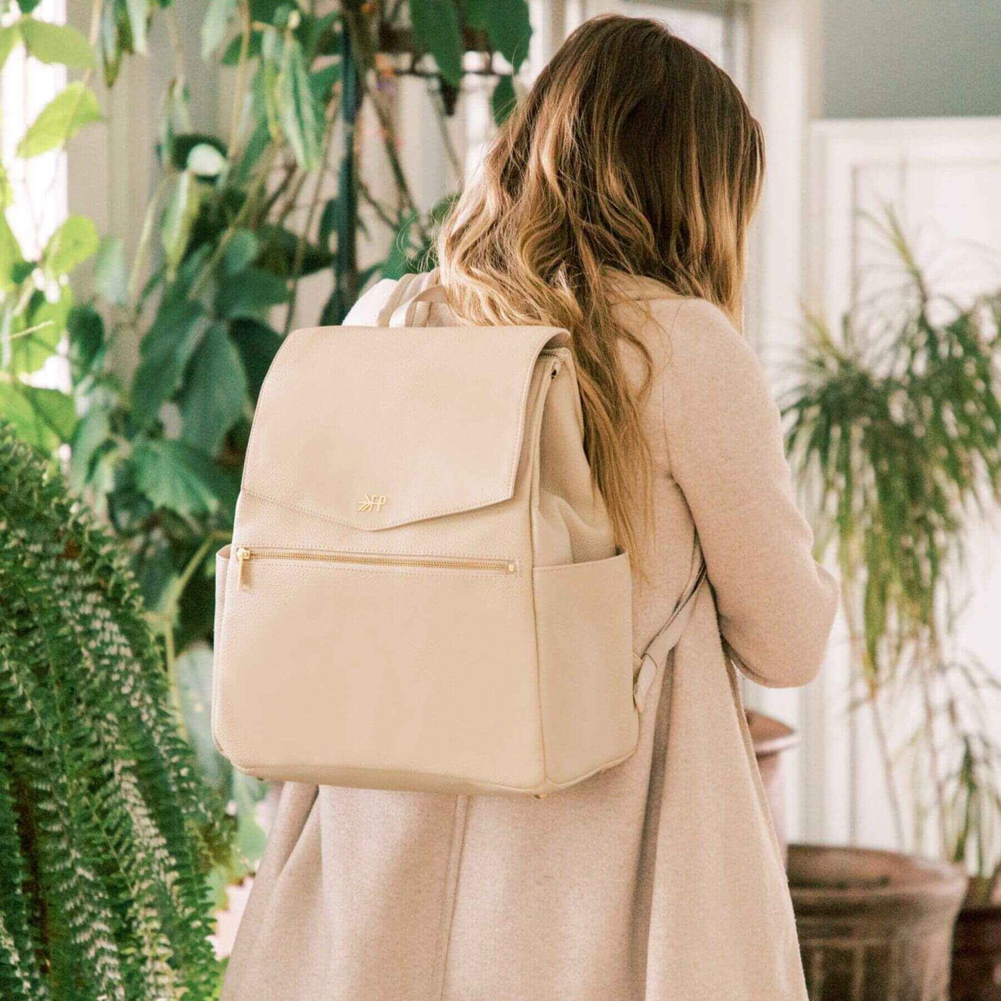 Woman wearing Freshly Picked Birch Classic Diaper Bag II in a plant-filled room