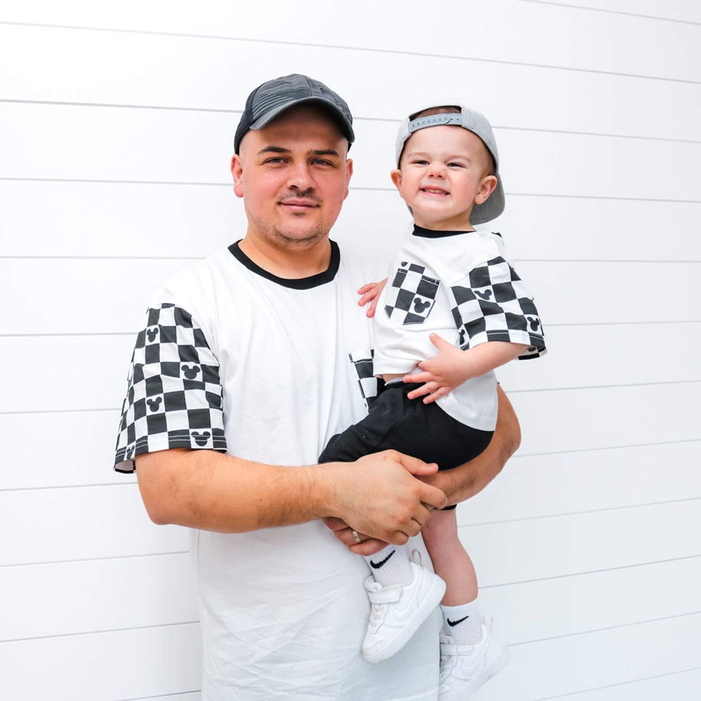 Man holding a child both wearing Sweet P Baby Co. Black Checkered Pocket Toddler & Kids T Shirt against a white background