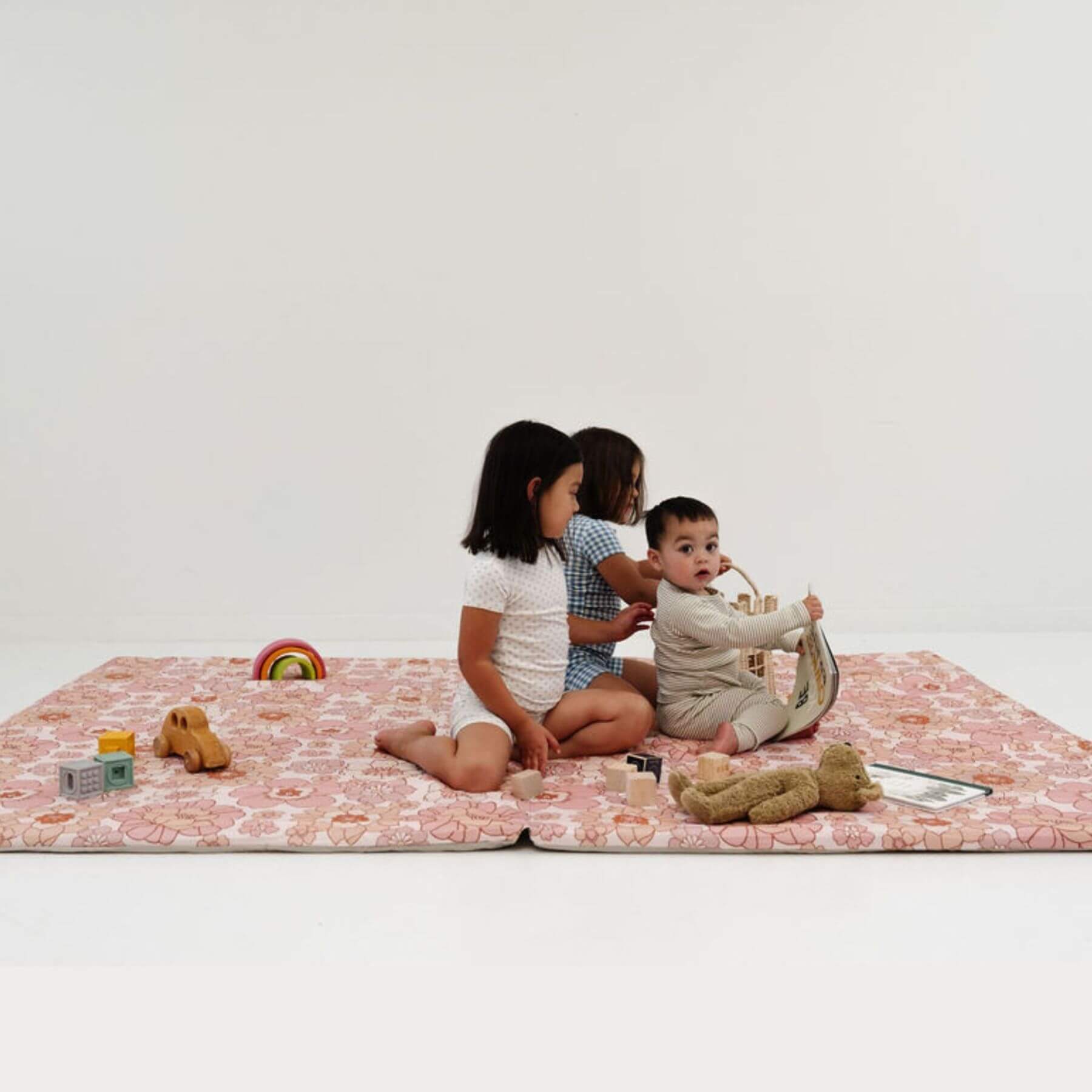 Three children playing on Toki Mats Blooms Organic Cotton Mat with toys against a white background