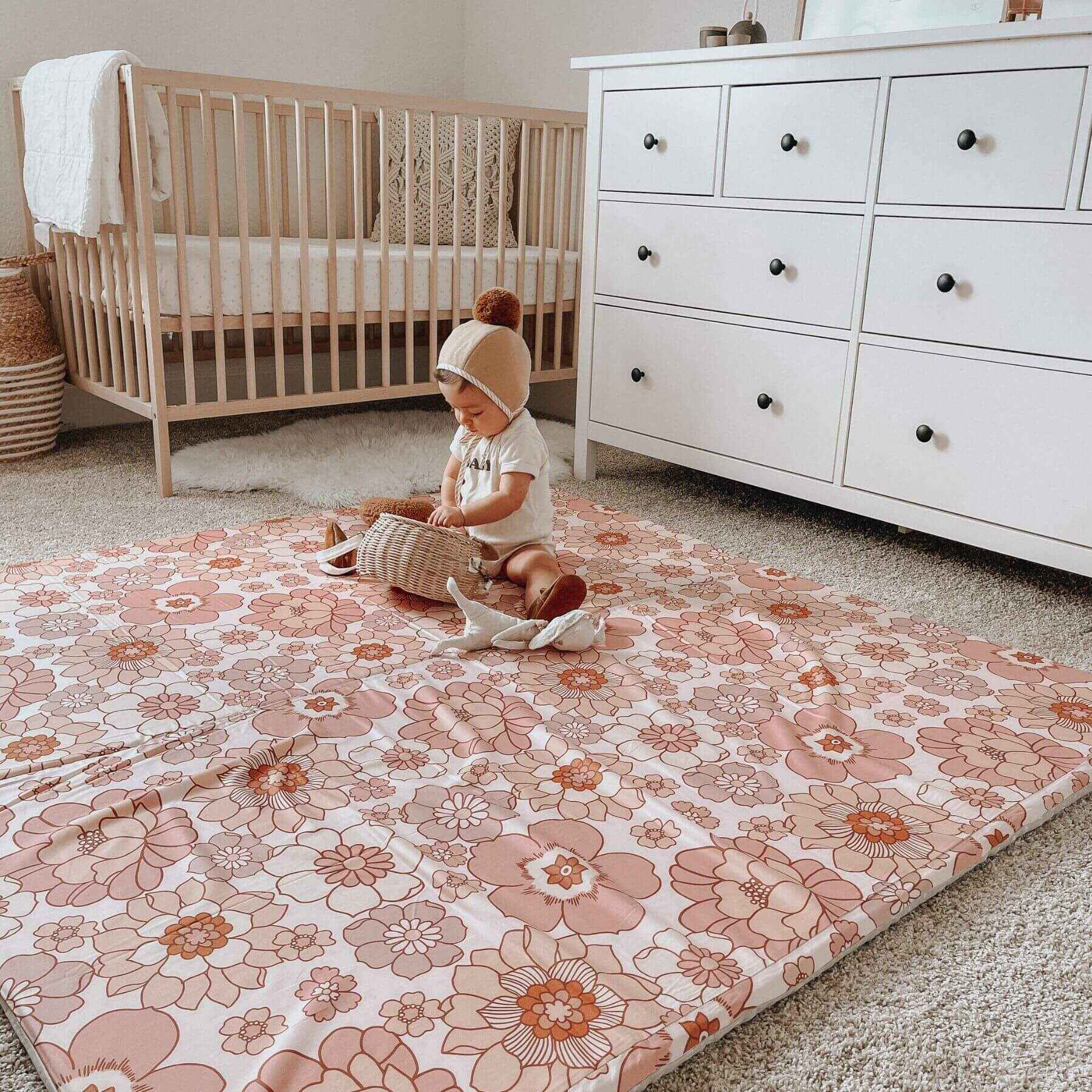 Child playing on Toki Mats Blooms Organic Cotton Mat in a nursery with a crib and dresser.