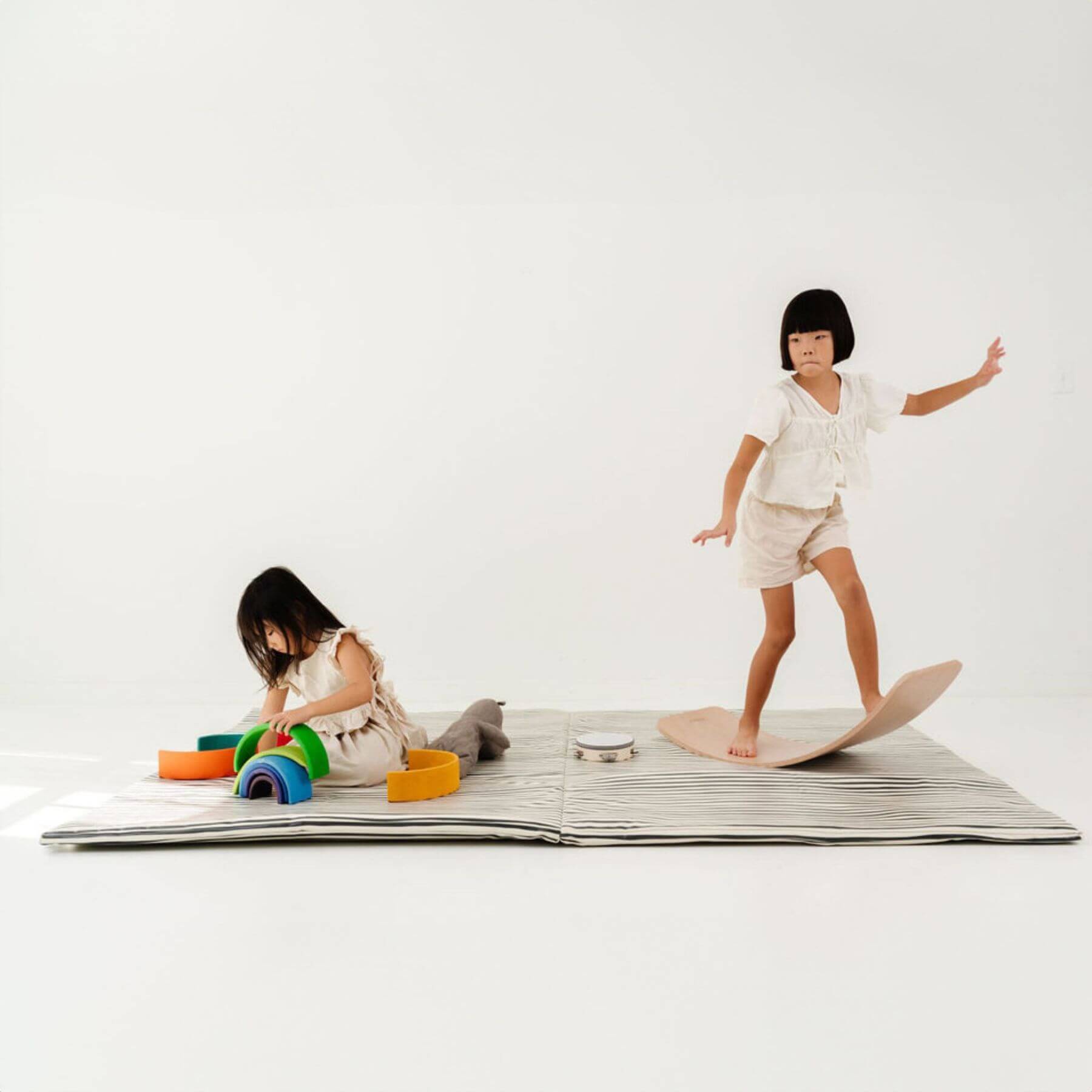 Two children playing on Toki Kids Bold Stripe Vegan Leather Mat with colorful toys and a surfboard.