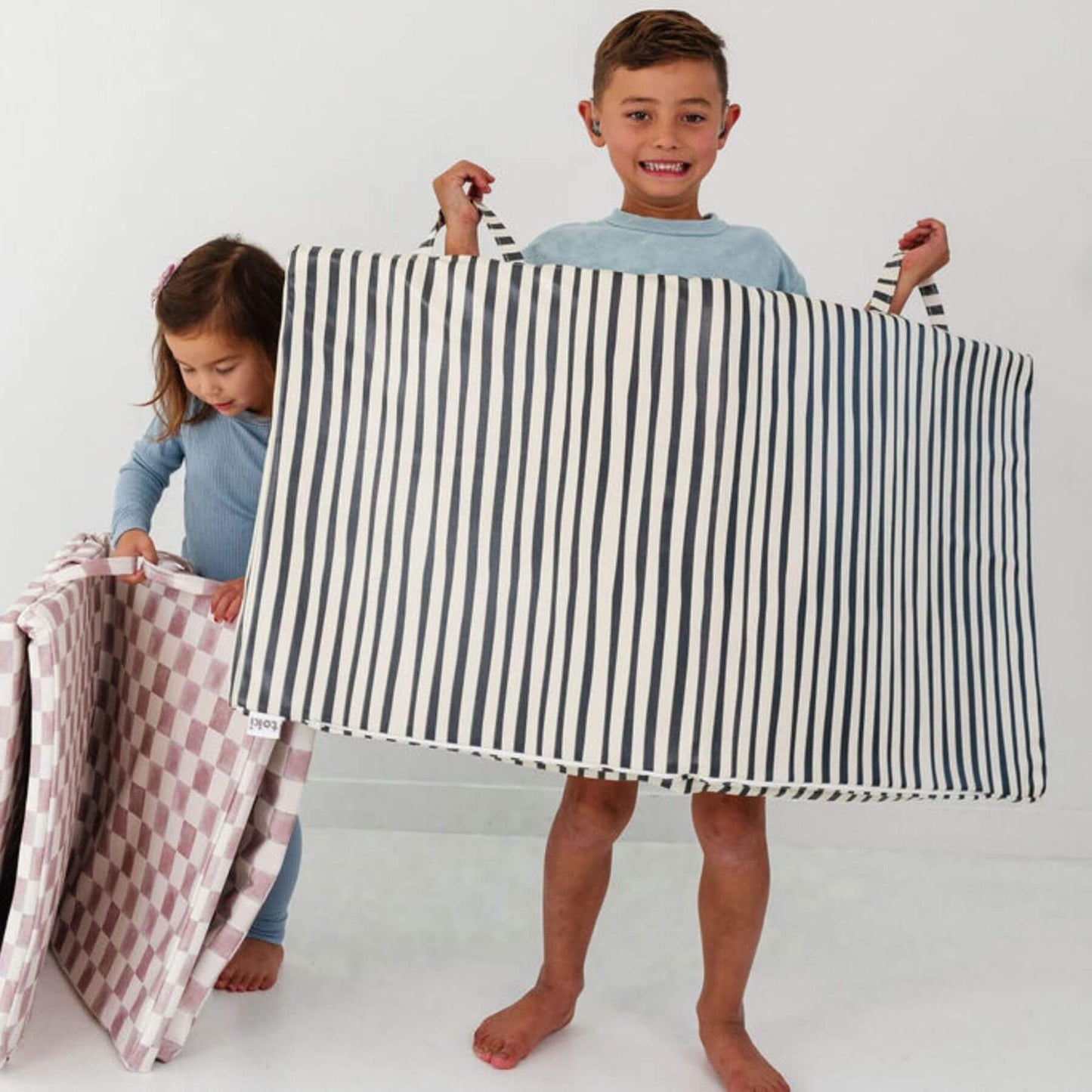 Two children holding a black and white striped mat against a white background