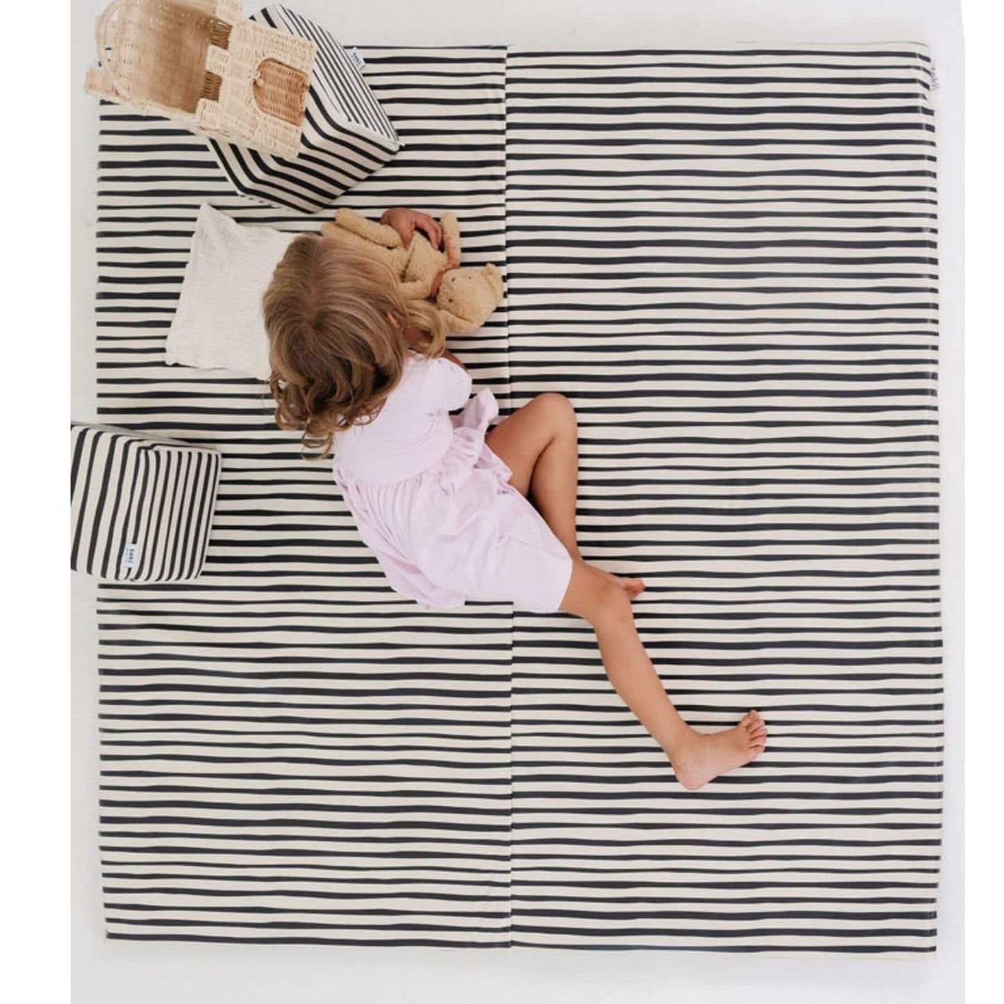 Child sitting on Toki Kids Bold Stripe Vegan Leather Mat with a teddy bear