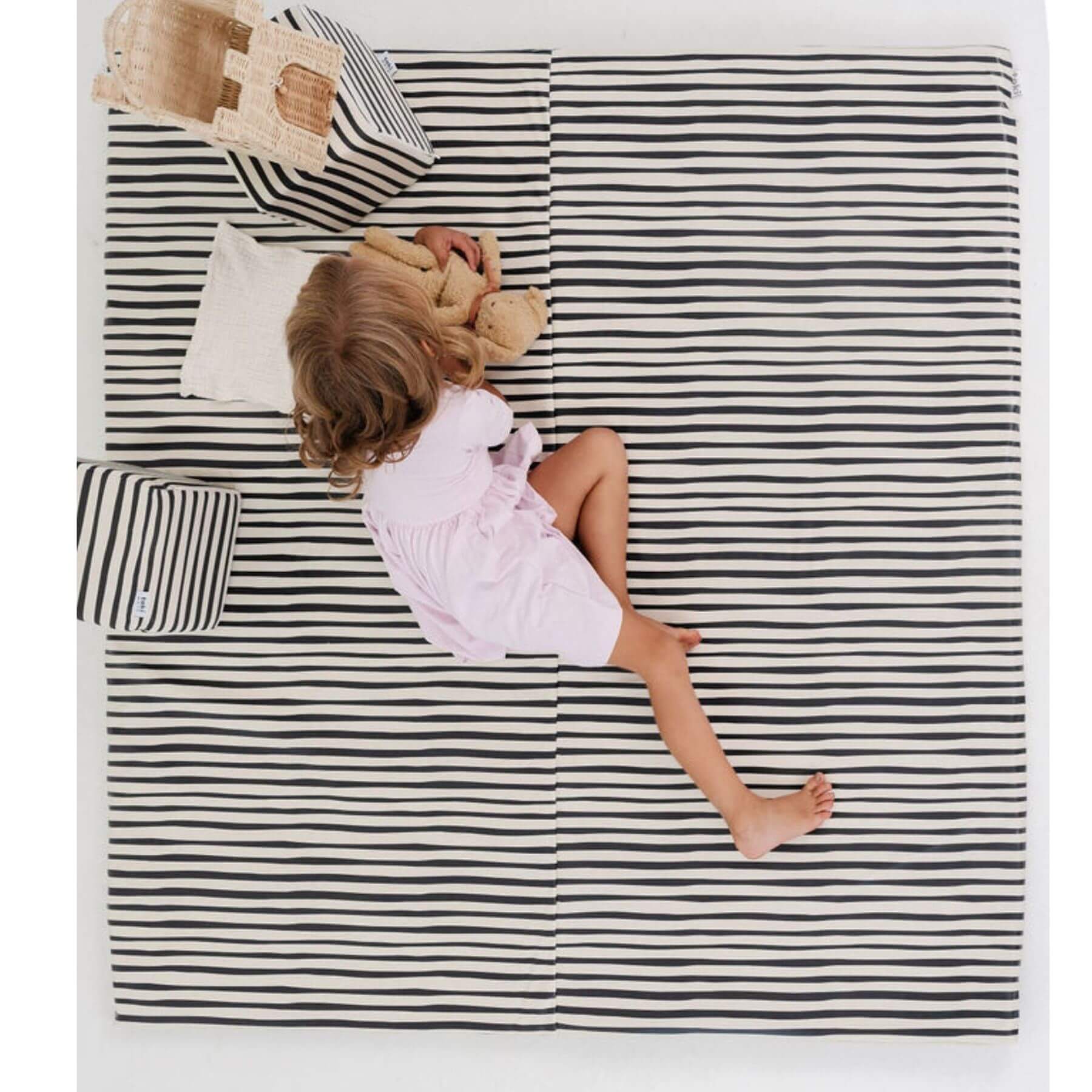 Child sitting on Toki Kids Bold Stripe Vegan Leather Mat with a teddy bear
