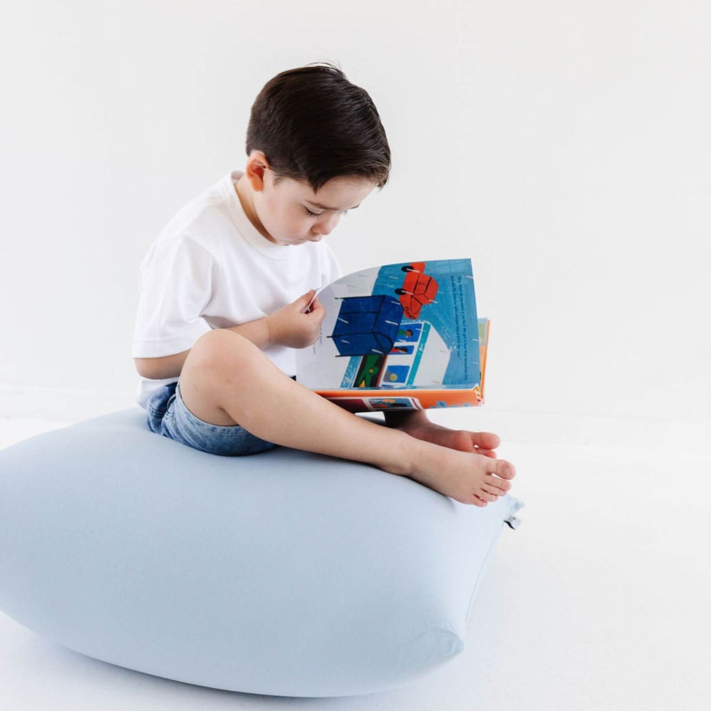 Child sitting on Toki Kids Breeze Bean Bag reading a book against a white background