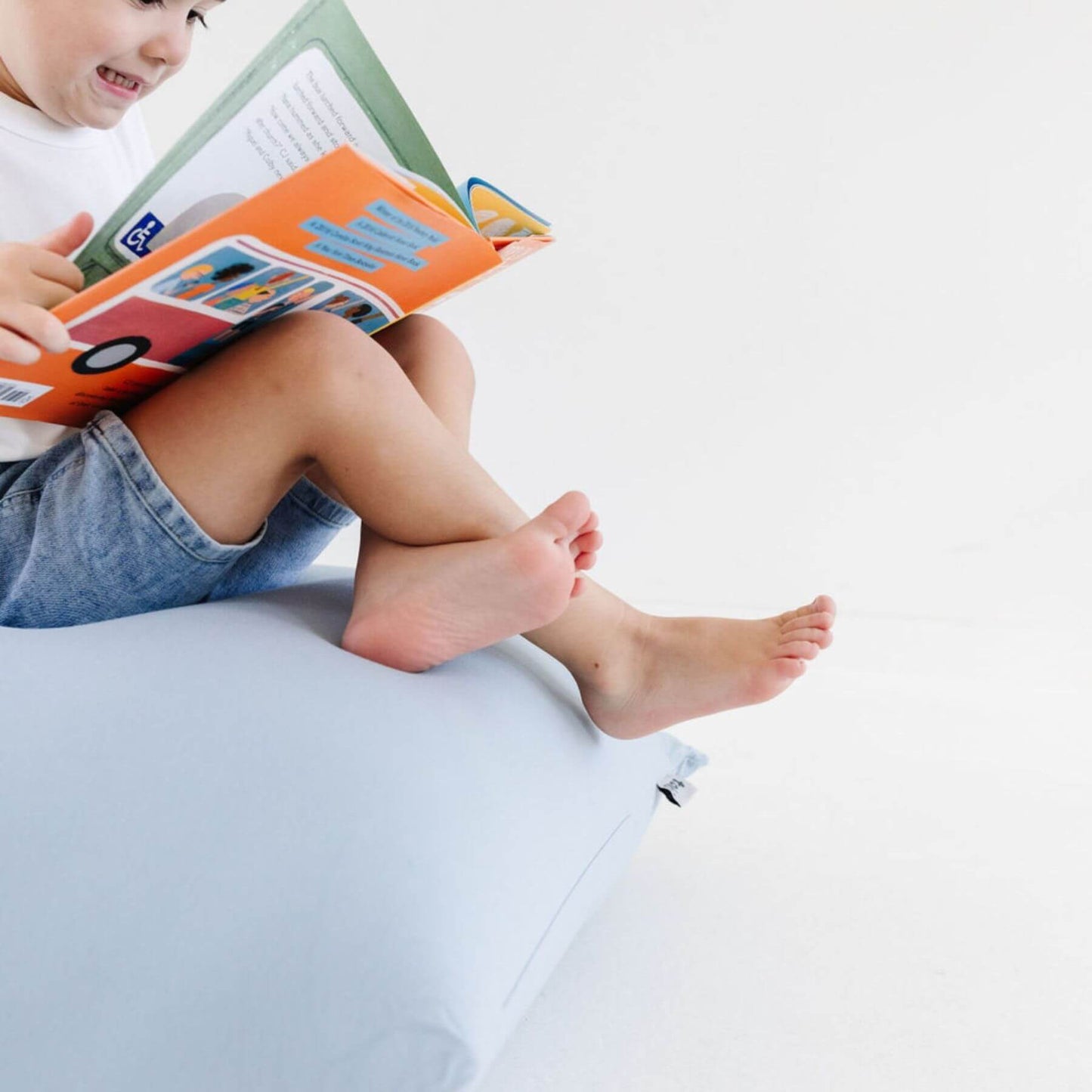 A child sitting on Toki Kids Breeze Bean Bag, reading an open colorful book.