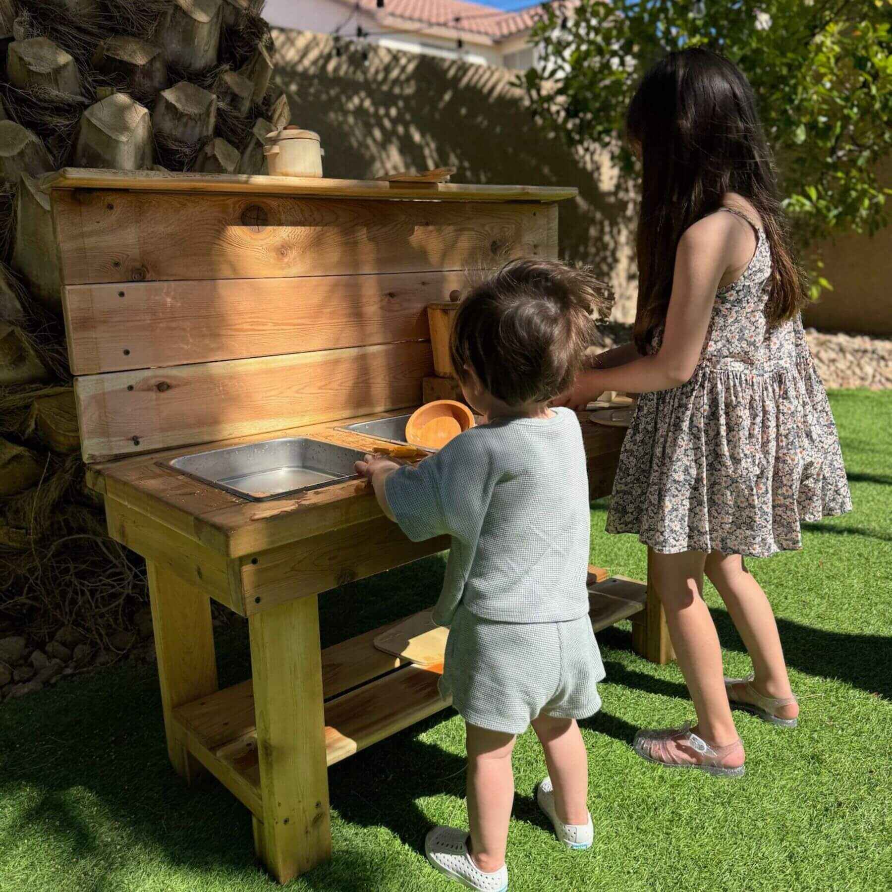 Two children playing with Bunny Hopkins Mud Kitchen outdoors.