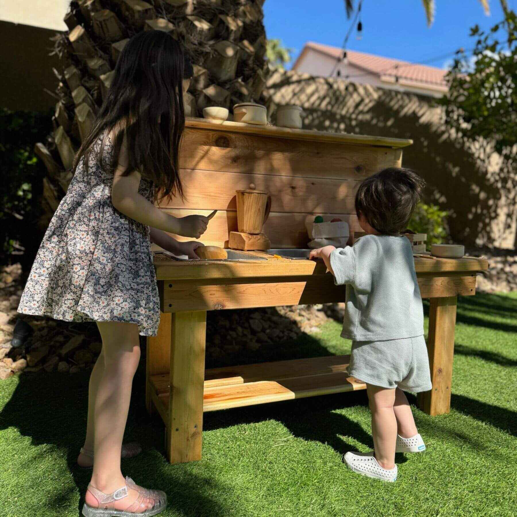 Two children playing at Bunny Hopkins Mud Kitchen with pots and pans.
