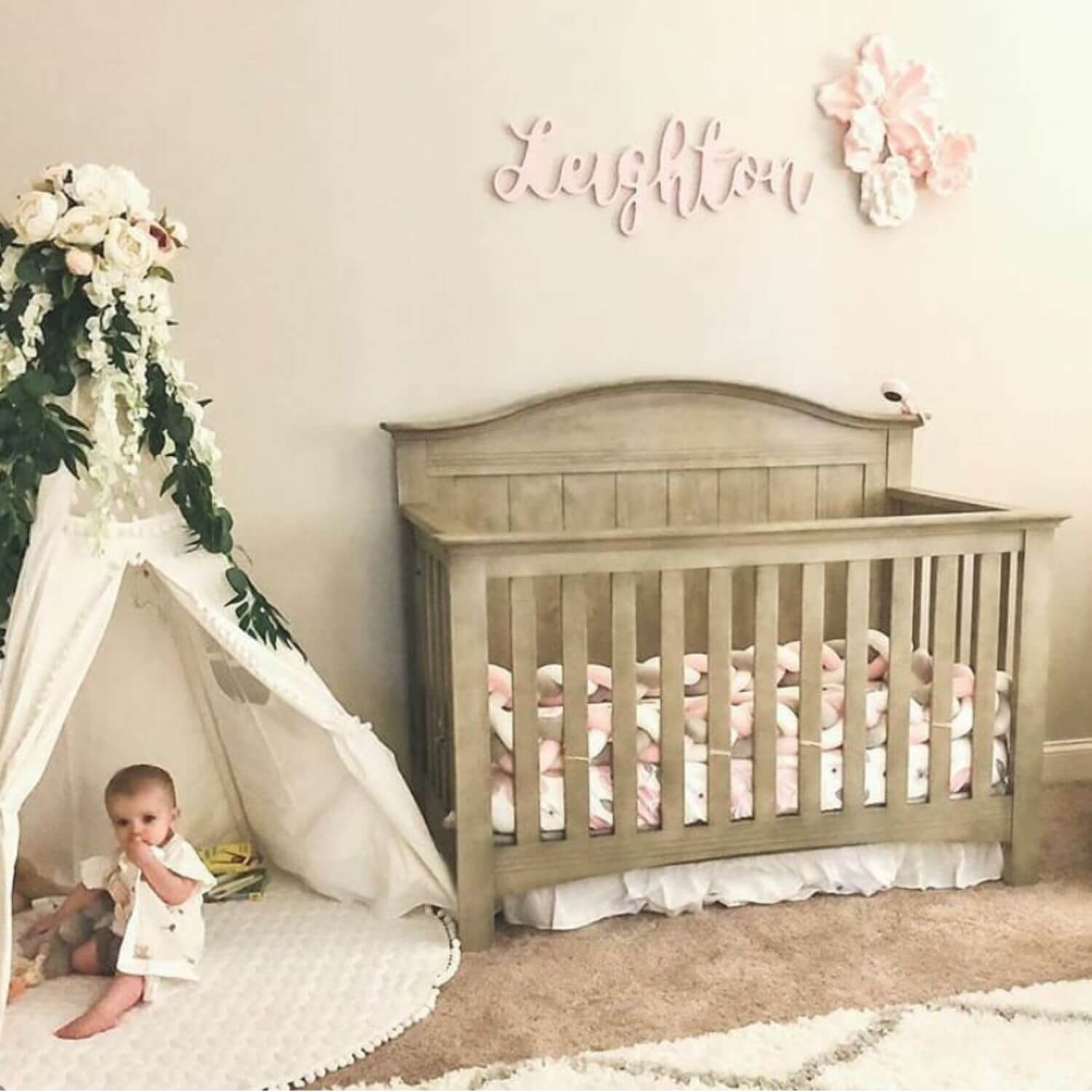 Baby crib with a child peeking out from a teepee in a nursery setting.