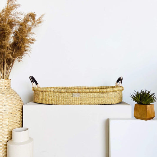 Decorative setup with Plum+Sparrow Changing Basket Brown+Cream Handle, vase, and plant on a white surface.