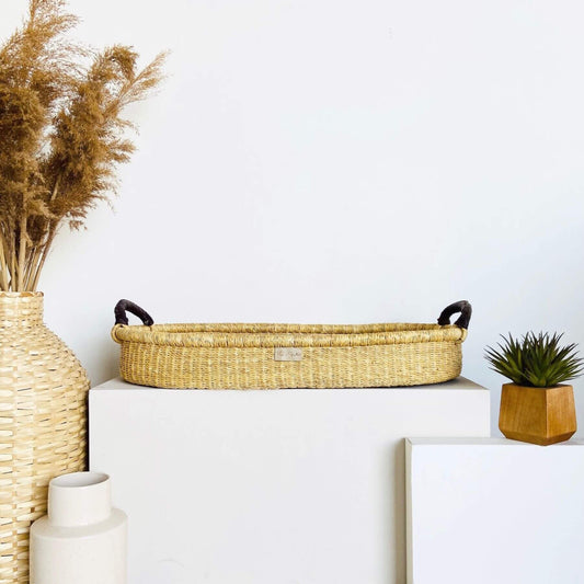 Plum+Sparrow Changing Basket Brown Handle, vase with dried plants, and small plant on a white surface.
