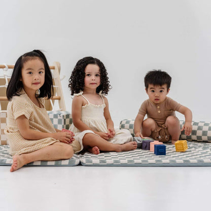 Three children sitting on Toki Kids Checker Matcha Organic Cotton Mat with colorful blocks around them.