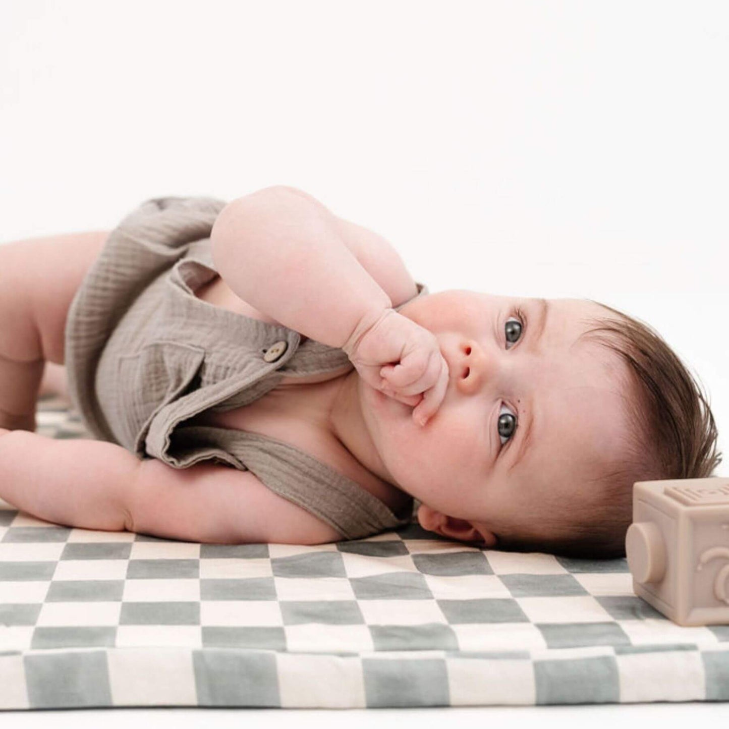 Baby lying on Toki Kids Checker Matcha Organic Cotton Mat with a wooden block