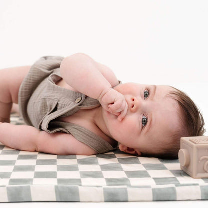 Baby lying on Toki Kids Checker Matcha Organic Cotton Mat with a wooden block