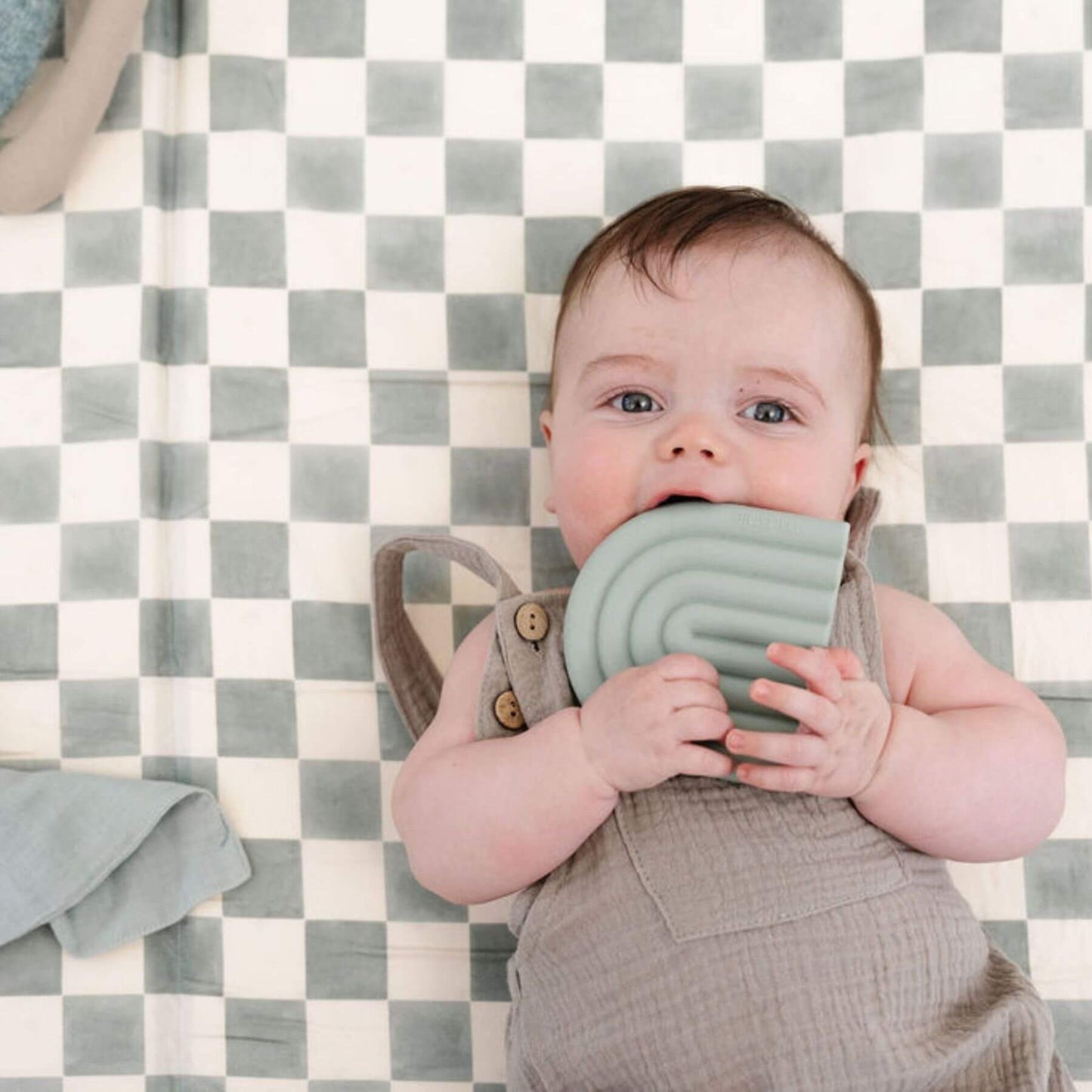 Baby holding a green teething ring on Toki Kids Checker Matcha Organic Cotton Mat