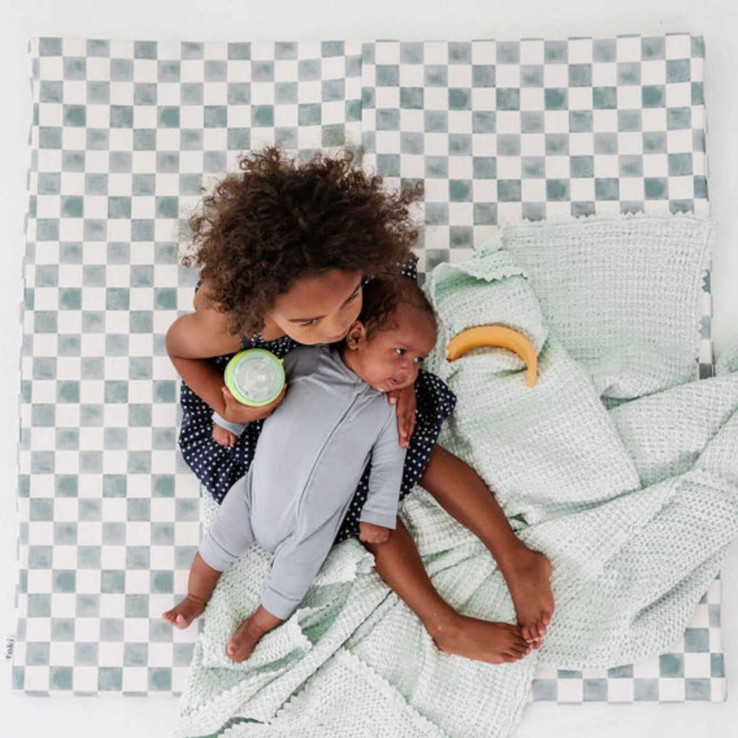 Two children playing on a checkered mat with a green blanket.