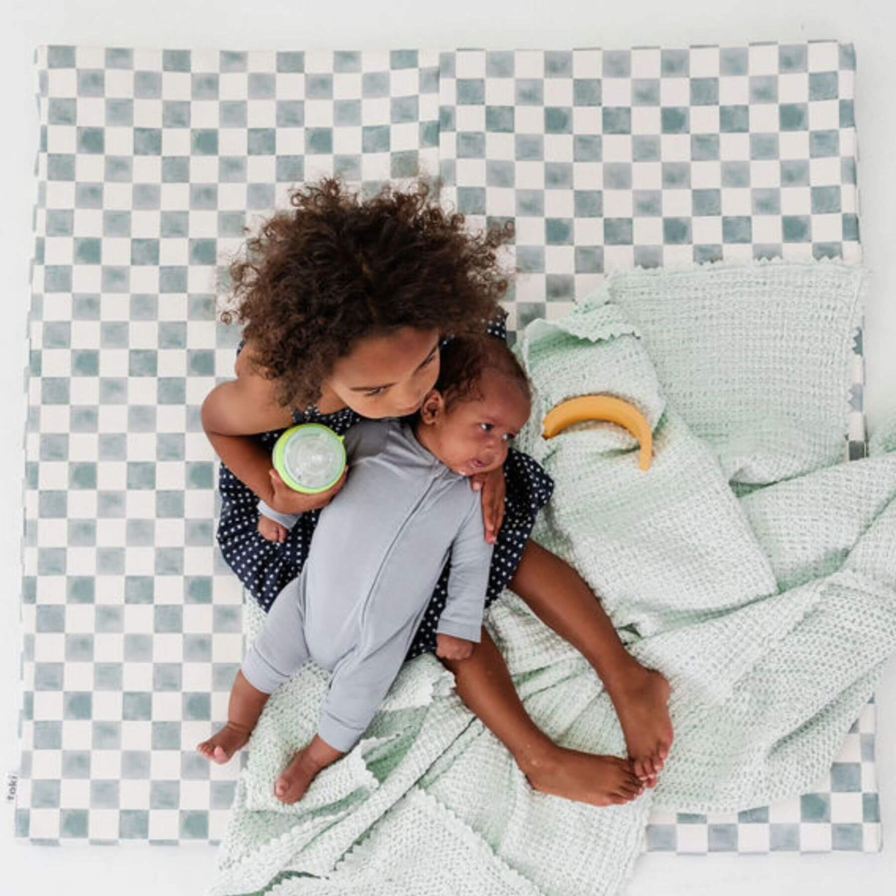 Two children playing on a checkered mat with a green blanket.
