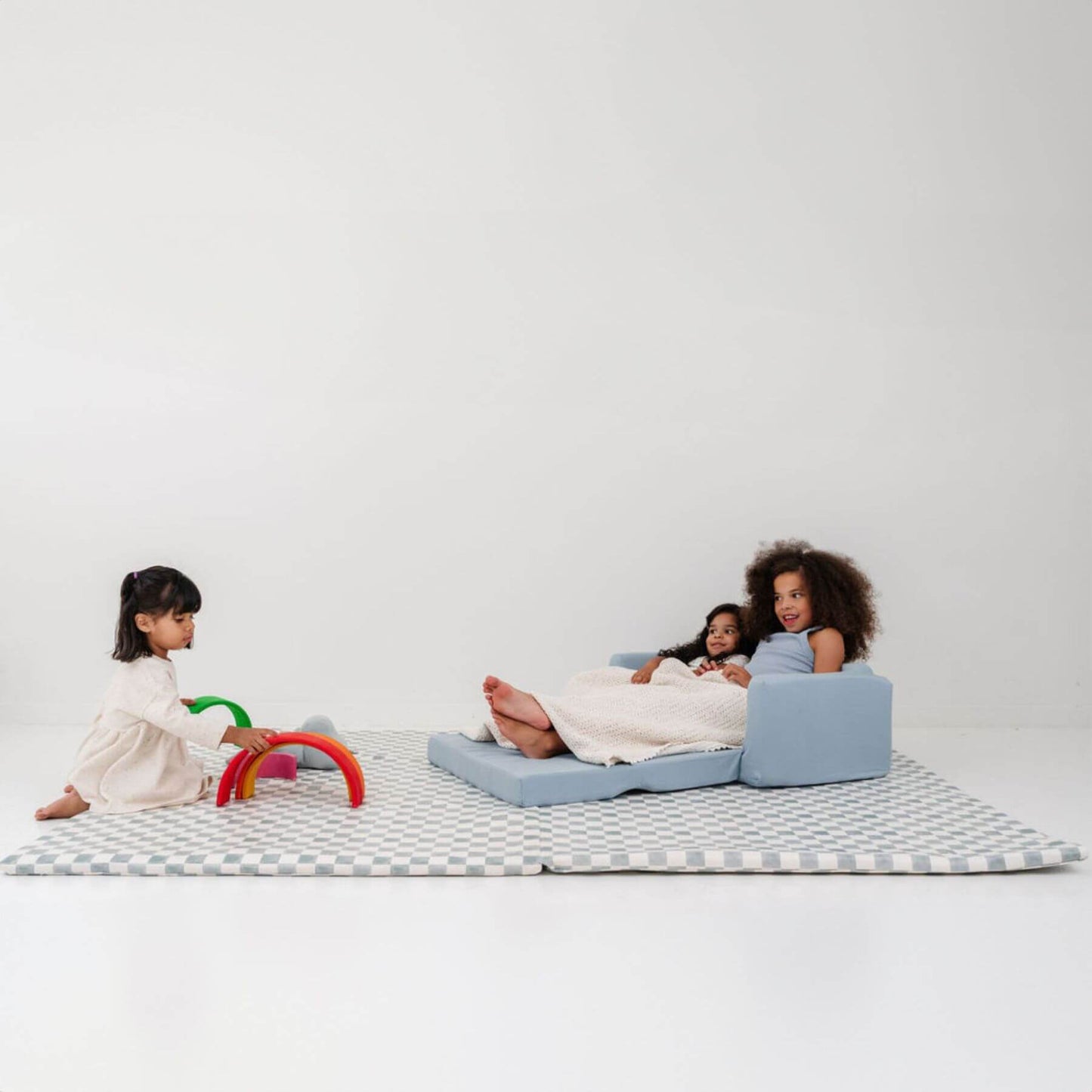 Children playing on a checkered mat with a blue sofa against a white background