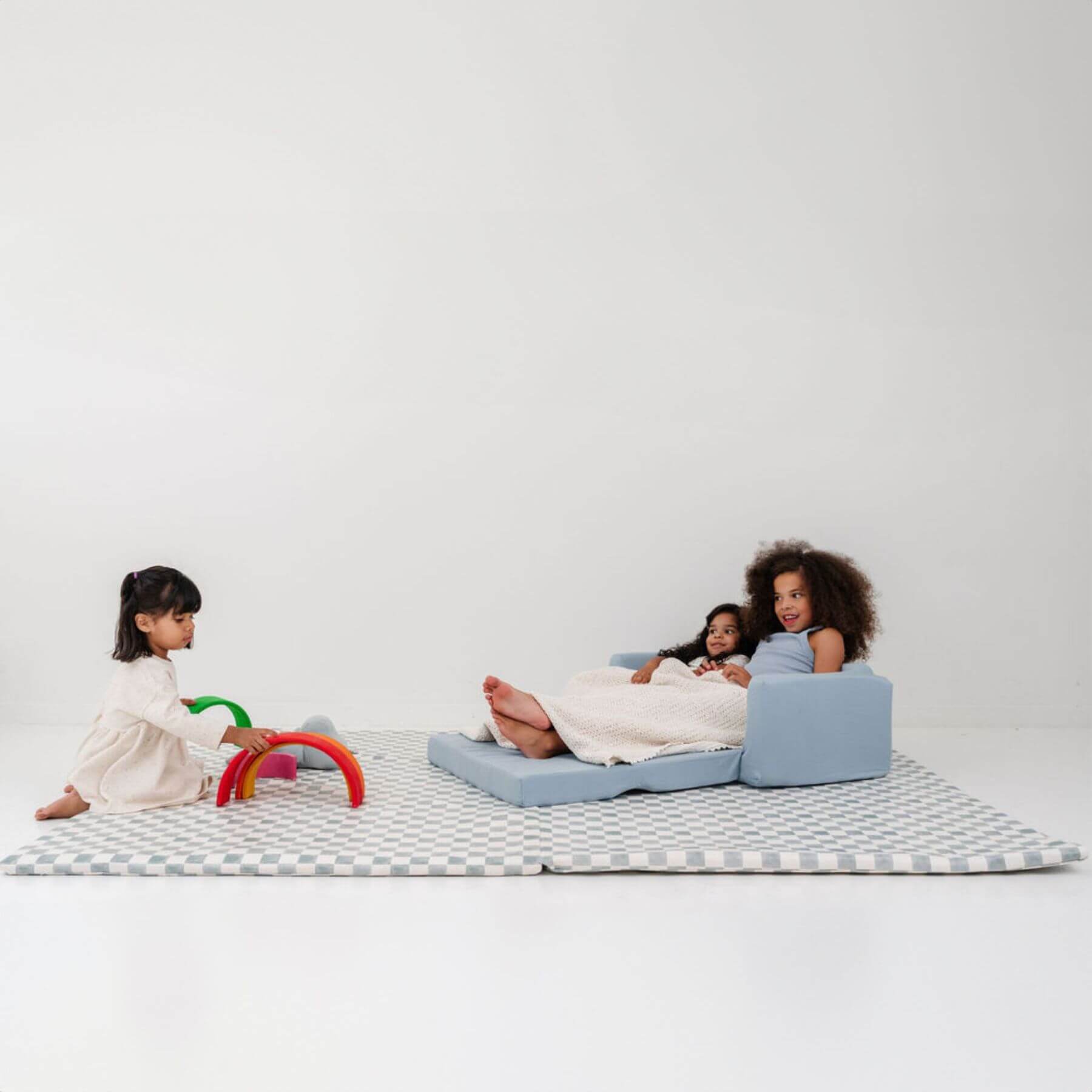 Children playing on a checkered mat with a blue sofa against a white background